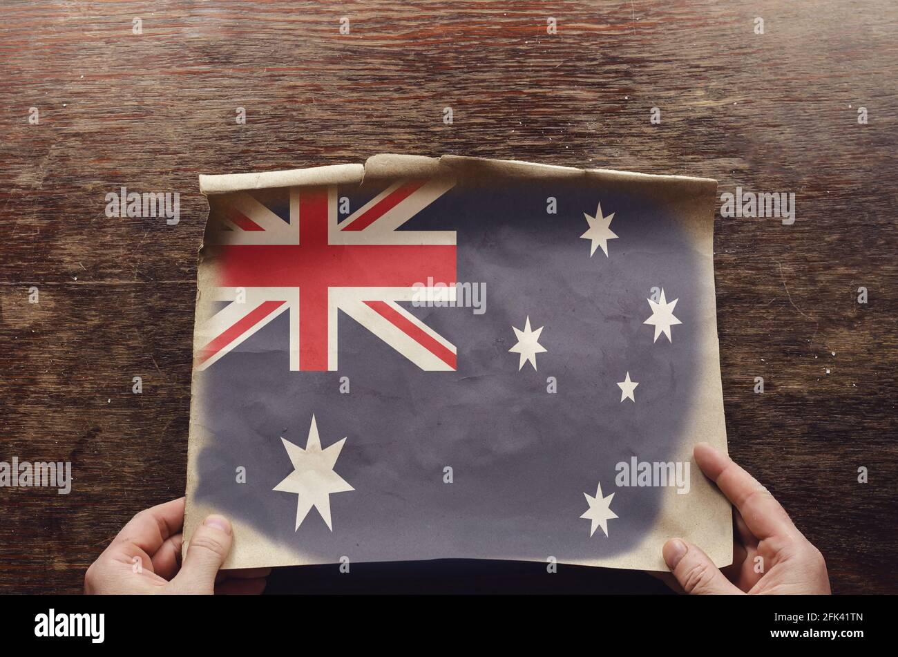 An old, shabby piece of paper with an Australian flag on it rests on the scratched table. The man's hands hold the unfolded piece of parchment to the Stock - Alamy