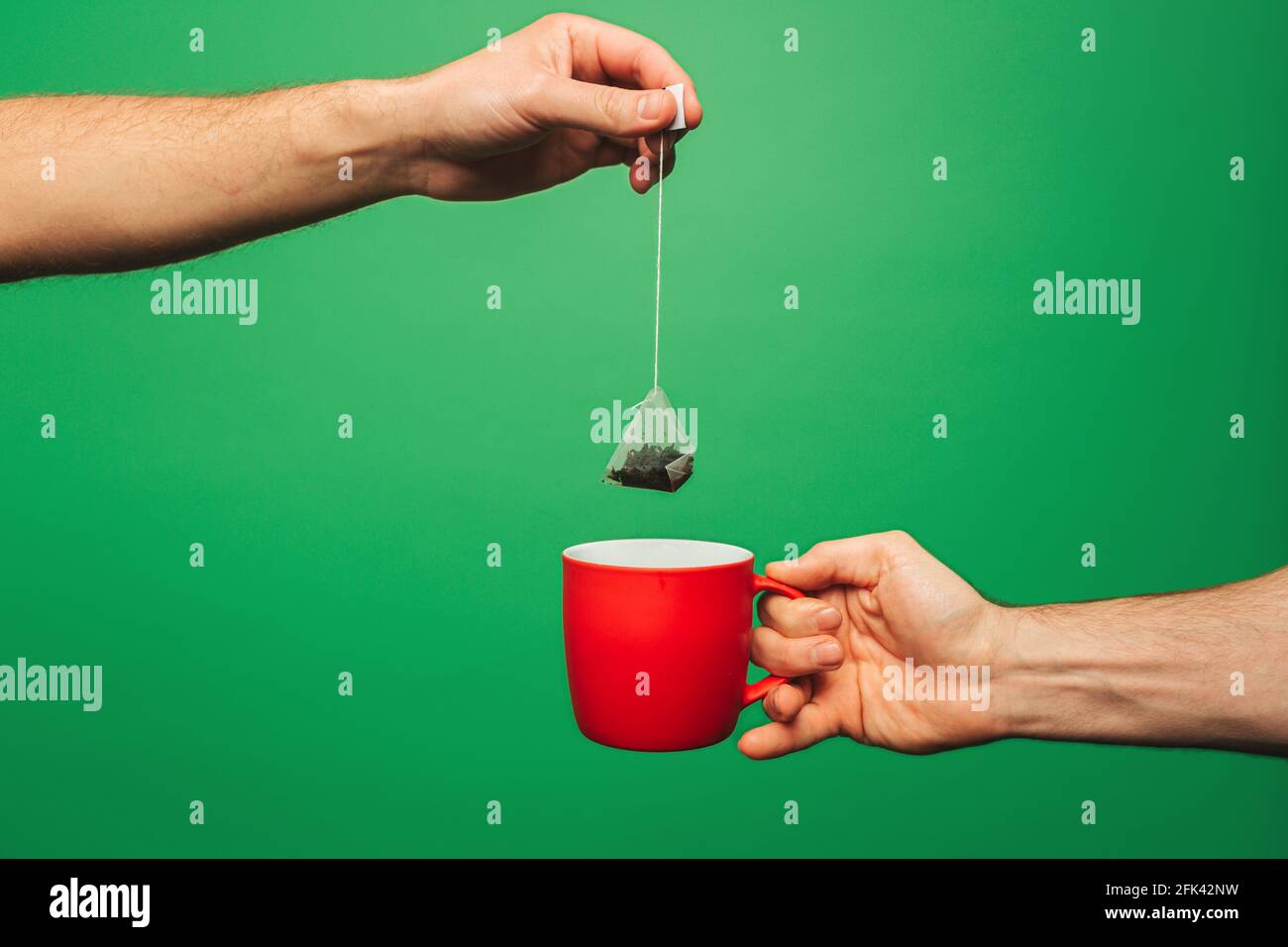 Close up man is preparing tea, isolated on green background Stock Photo