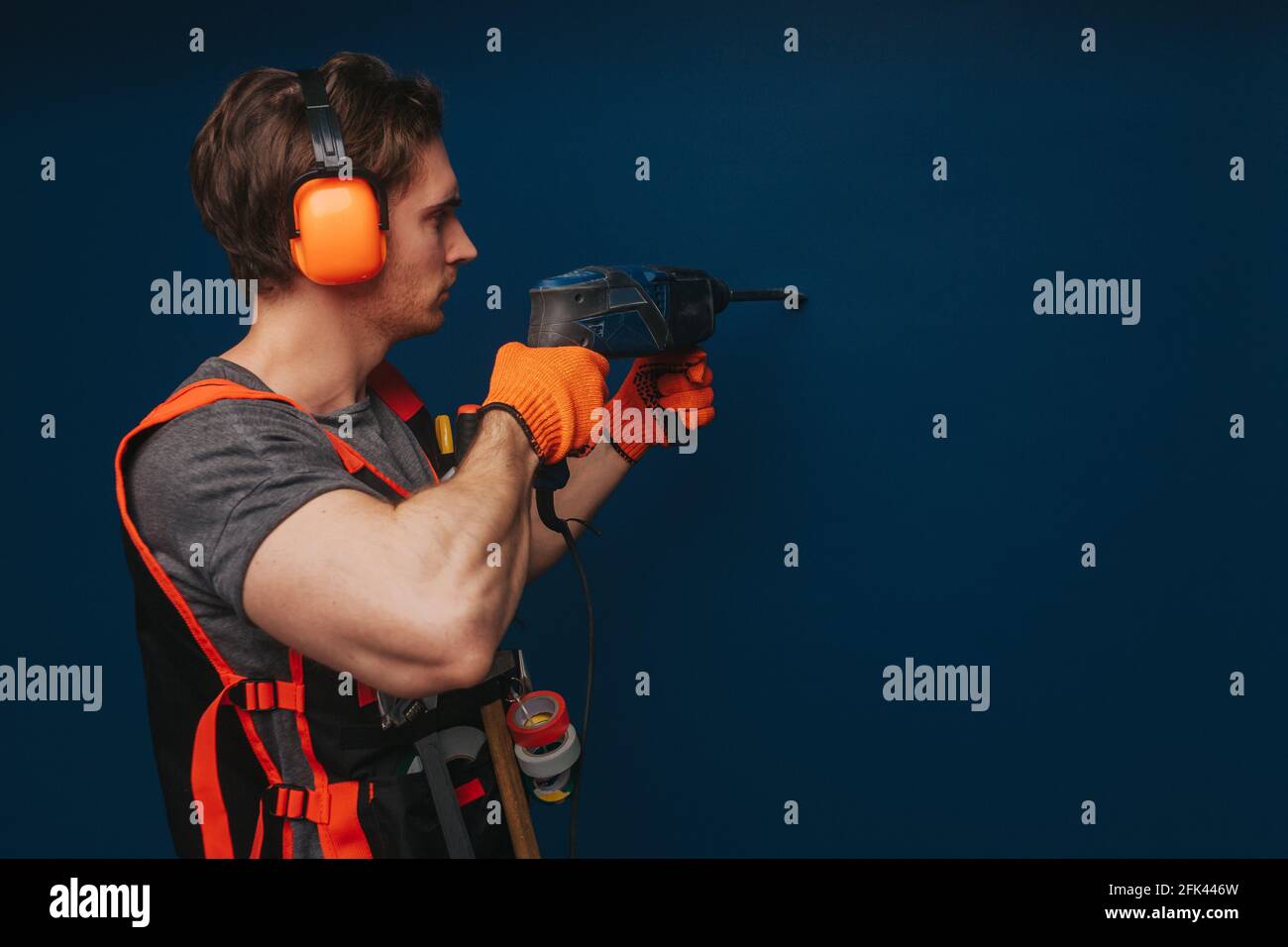 Young builder is drilling the wall, isolated over blue background Stock Photo