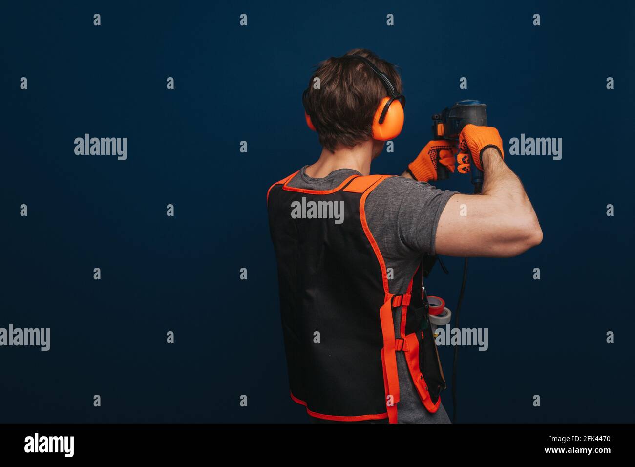 Young builder is drilling the wall, isolated over blue background Stock Photo