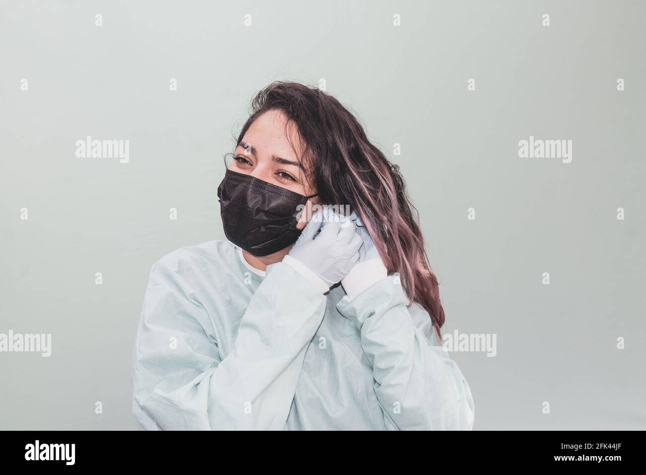 Closeup of an attractive cheerful female nurse in a black facemask fixing her earring Stock Photo