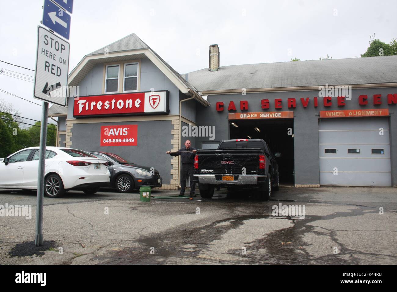 PORT JERVIS, NY, UNITED STATES - May 26, 2019: Firestone Auto Care Tire and Rubber Company with Cars in parking lot. Man is outside working. Driveway Stock Photo