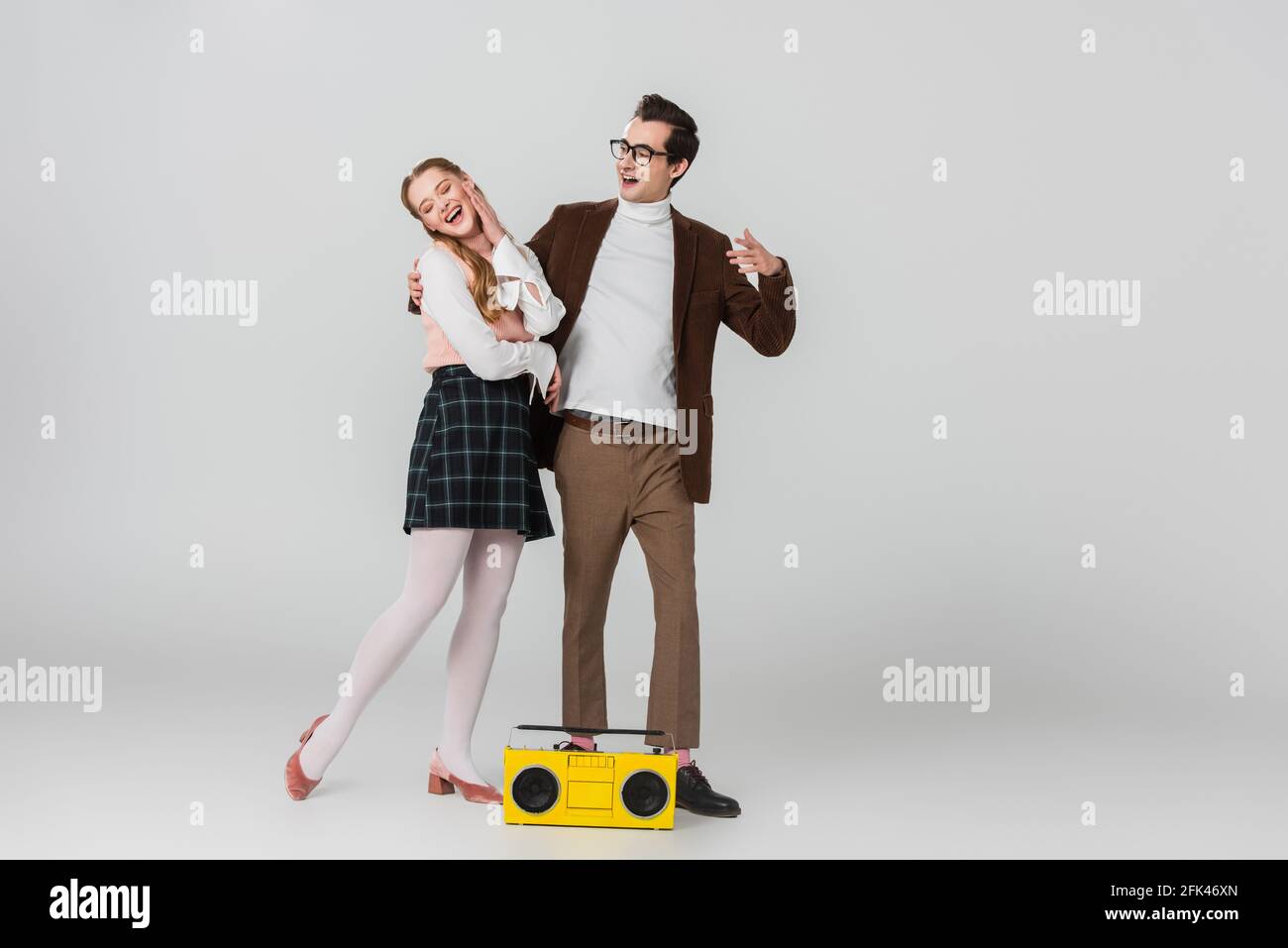smiling man embracing excited woman near vintage boombox on grey Stock Photo