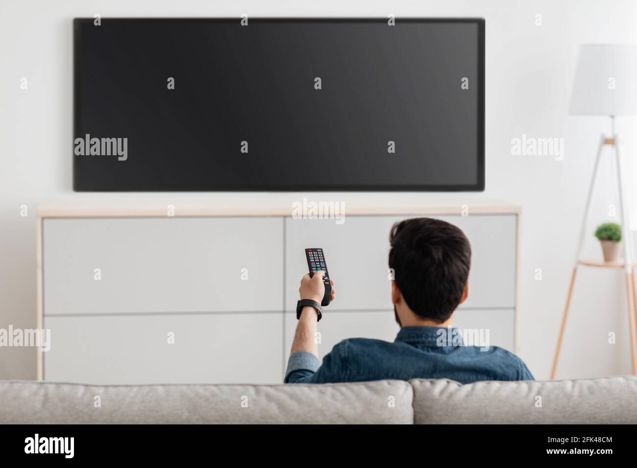 Man watching television, turning on plasma flatscreen TVset, pointing remote control at empty
