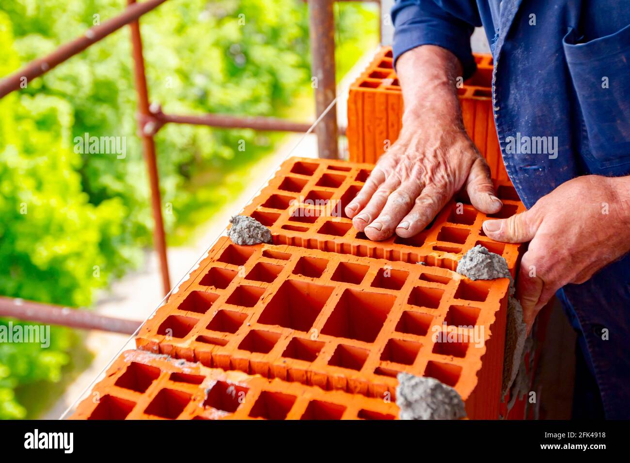 Mason, bricklayer worker is using red blocks to mount a wall next the
