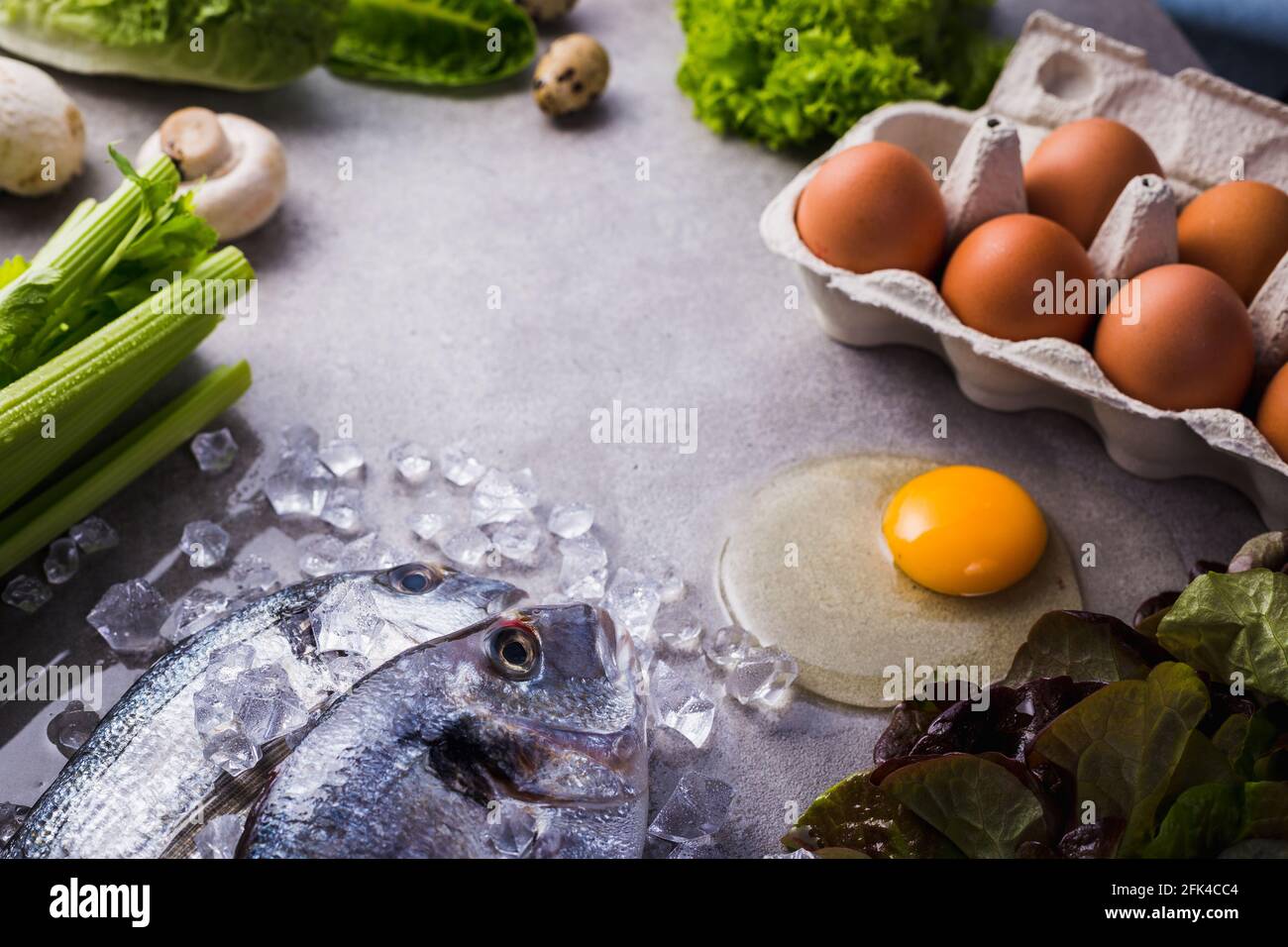 Frame of raw cooking ingredients for tasty and healthy food. Fresh dorado fish on ice, vegetables, eggs on gray concrete background top view. Stock Photo