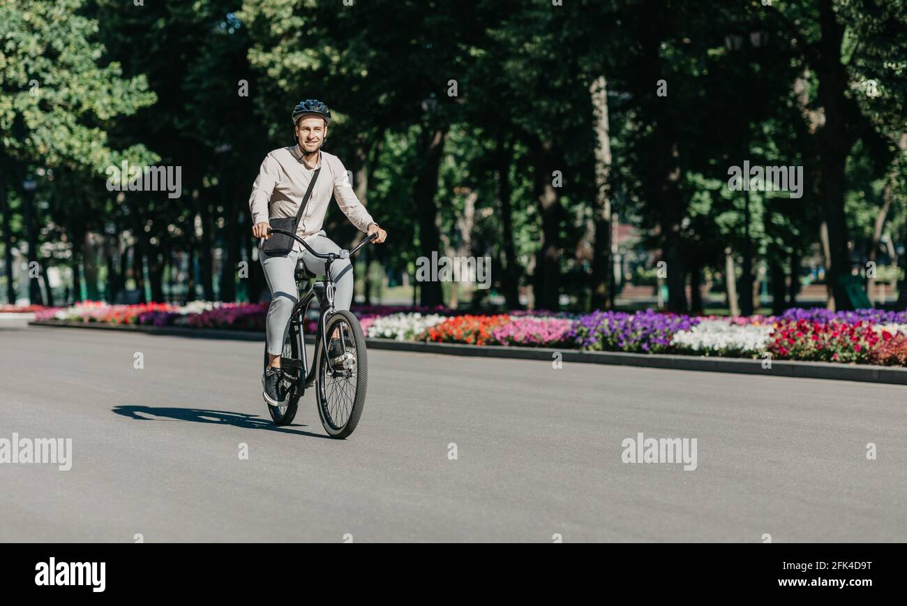 Cheerful young employee with helmet on utility bicycle rides to modern workplace Stock Photo