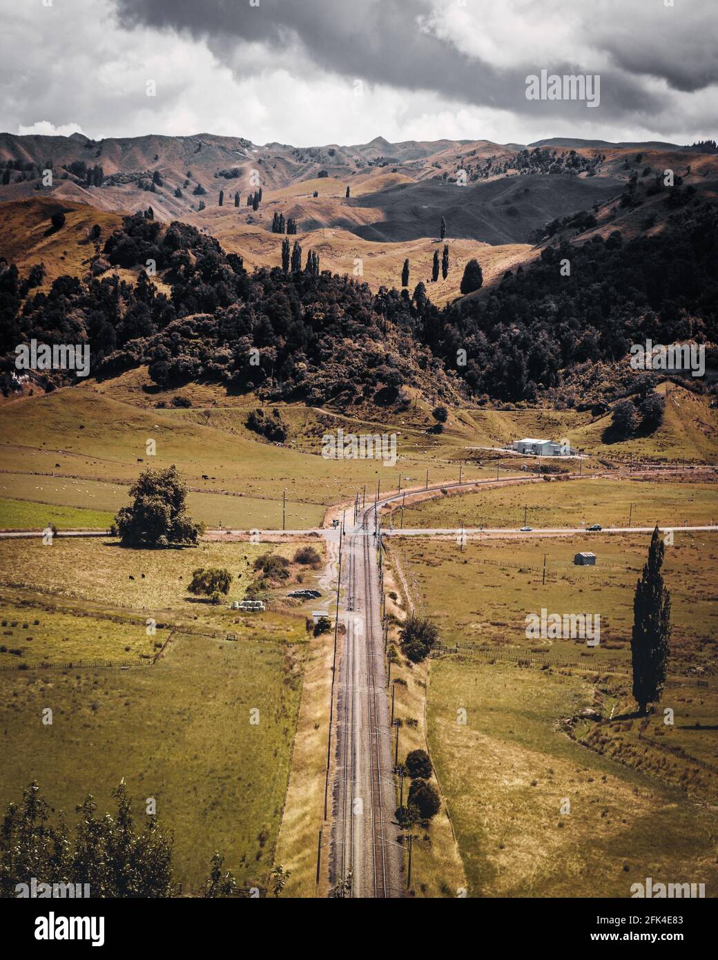 Vertical shot of a long road on the field against cloudy sky background ...