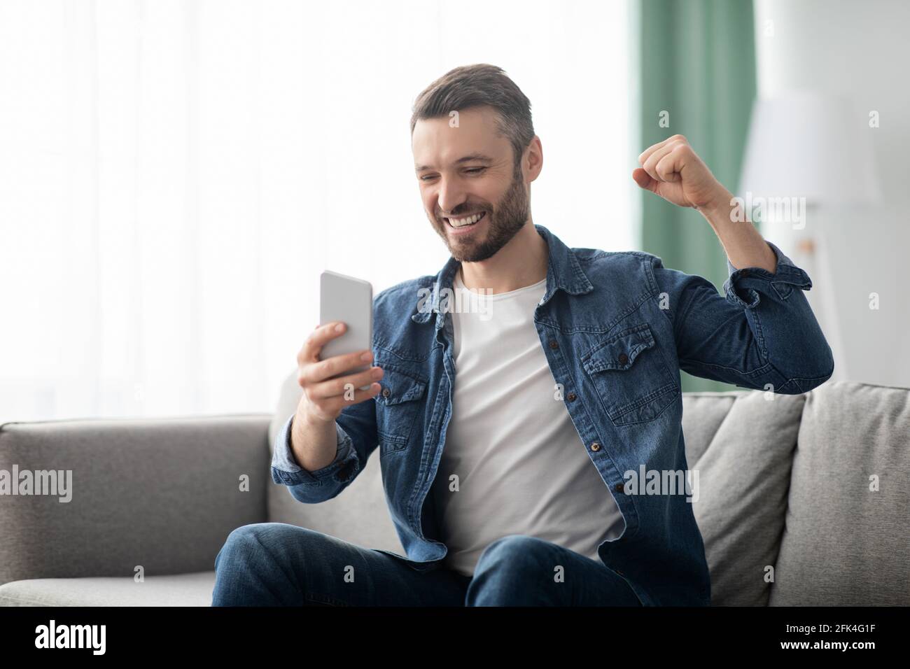 Emotional bearded man celebrating success, using mobile phone Stock Photo