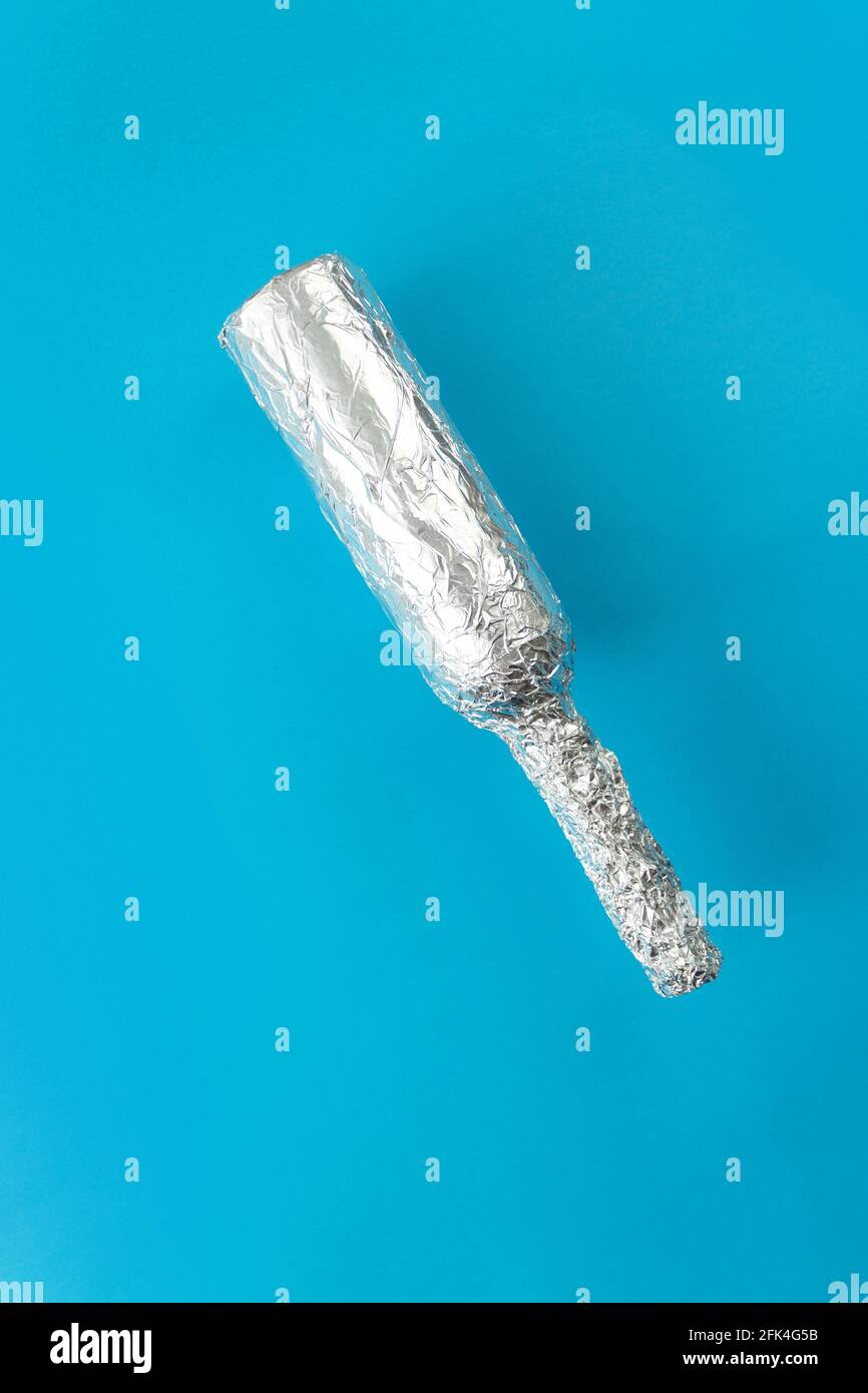 Tin foil wrapped bottle falling against a blue background Stock Photo