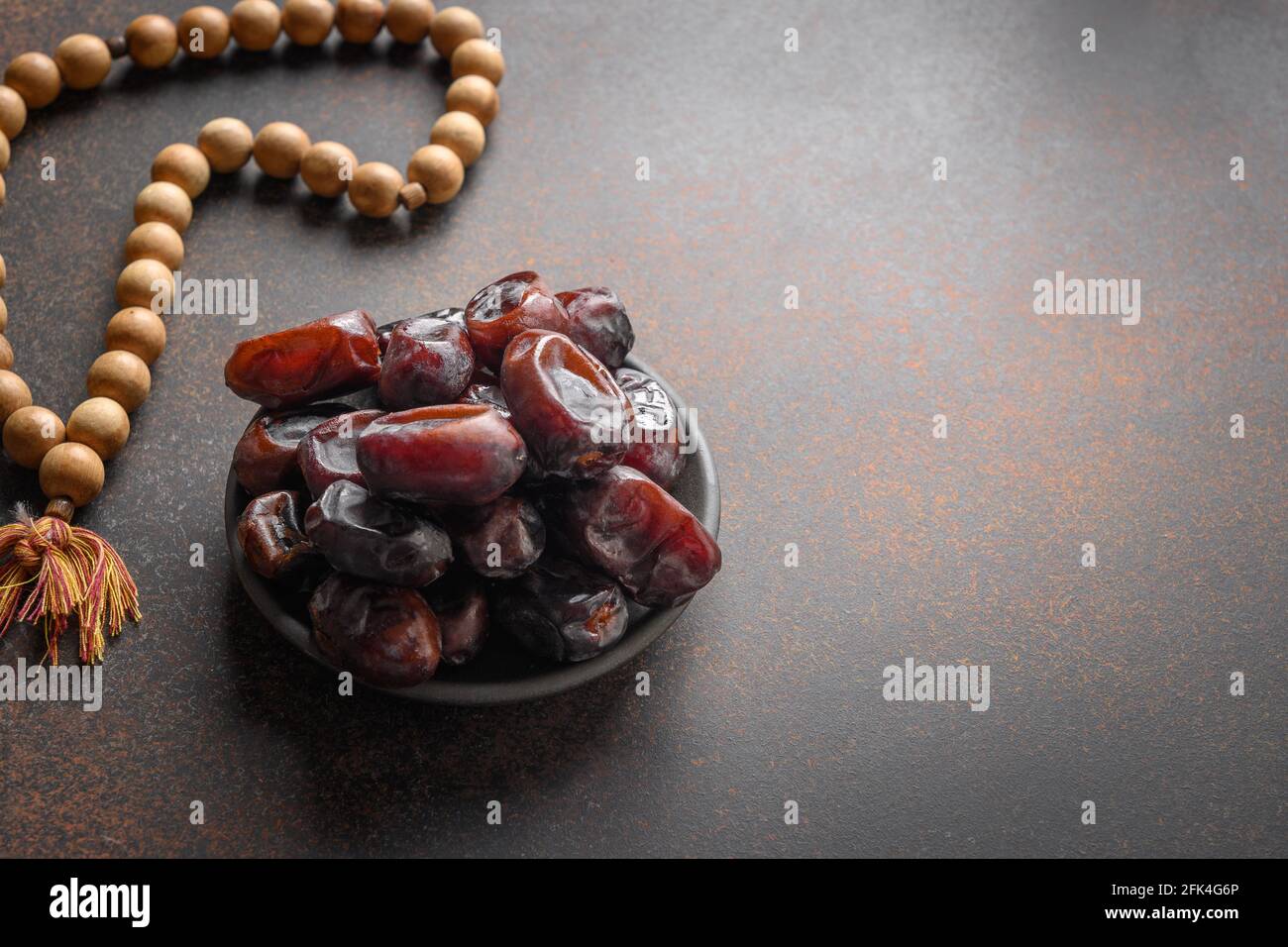 Ramadan. Wooden prayer beads and dates in bowl on brown. View from above. Eid Mubarak. Religious tradition. Stock Photo