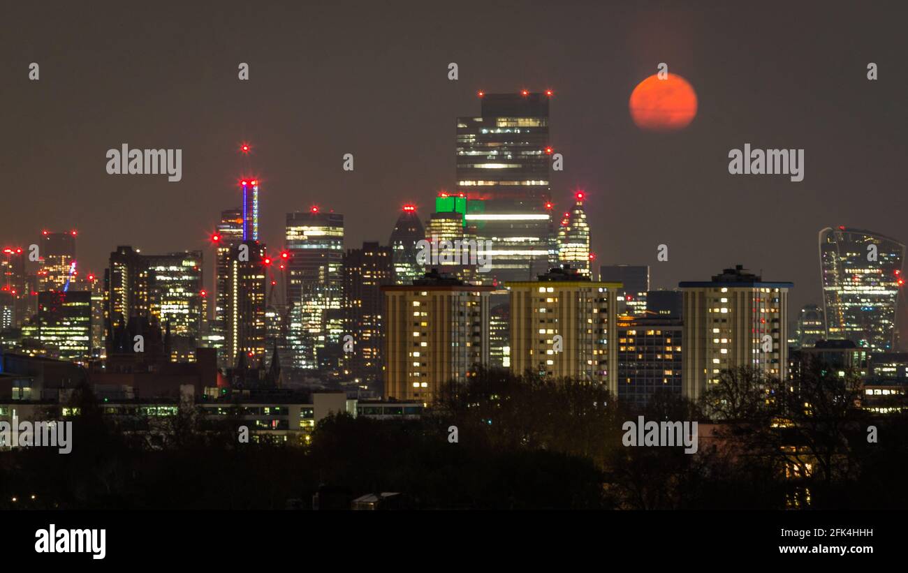 Celestial Event as the super pinkmoon rises through the clouds over London. Stock Photo