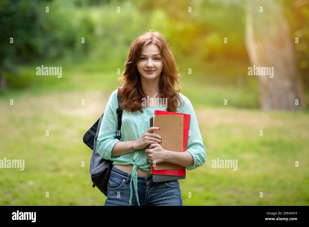 Attractive redhead student girl with backpack and workbooks posing at campus yard Stock Photo