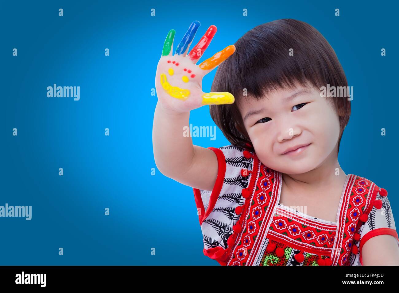 Adorable little asian (thai) girl painting her palm, colorful right hand raised up and painted with smiling face, some space for input text message. I Stock Photo