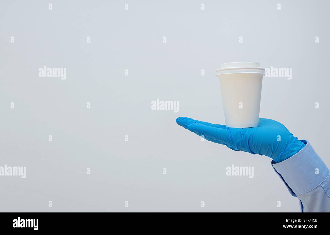 Hand in medical gloves carrying paper coffee cup coffee. Banner, copy space. Contactless delivery service during quarantine coronavirus pandemic. Take Stock Photo