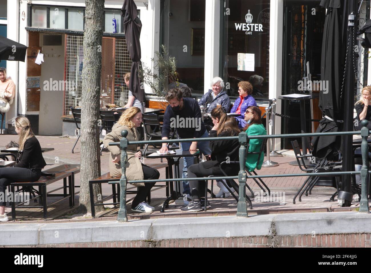 Amsterdam, Netherlands. 28th Apr, 2021. A waiter wearing a protective face mask shows menu to customers on a terrace of a café at the Prinsengracht canal in the center of Amsterdam amid the coronavirus pandemic on April 28, 2021 in Amsterdam, Netherlands. The Dutch government takes a major step today to relax the coronavirus lockdown, after six months of closure terraces and stores reopen but close at 6 pm across country. (Photo by Paulo Amorim/Sipa USA) Credit: Sipa USA/Alamy Live News Stock Photo