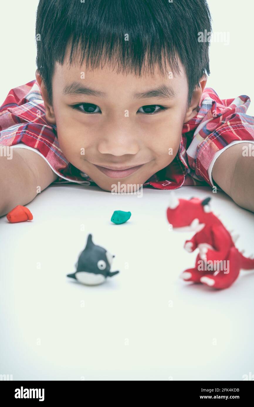 Asian handsome child smiling and show his works from clay, on white background. Strengthen the imagination of child. Vintage picture style. Selective Stock Photo
