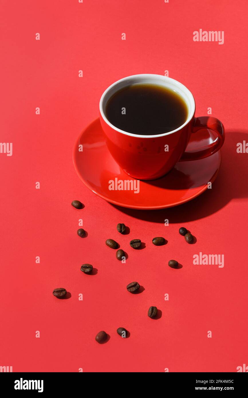 Red cup of coffee and beans on red background. Vertical format. Close up. Stock Photo
