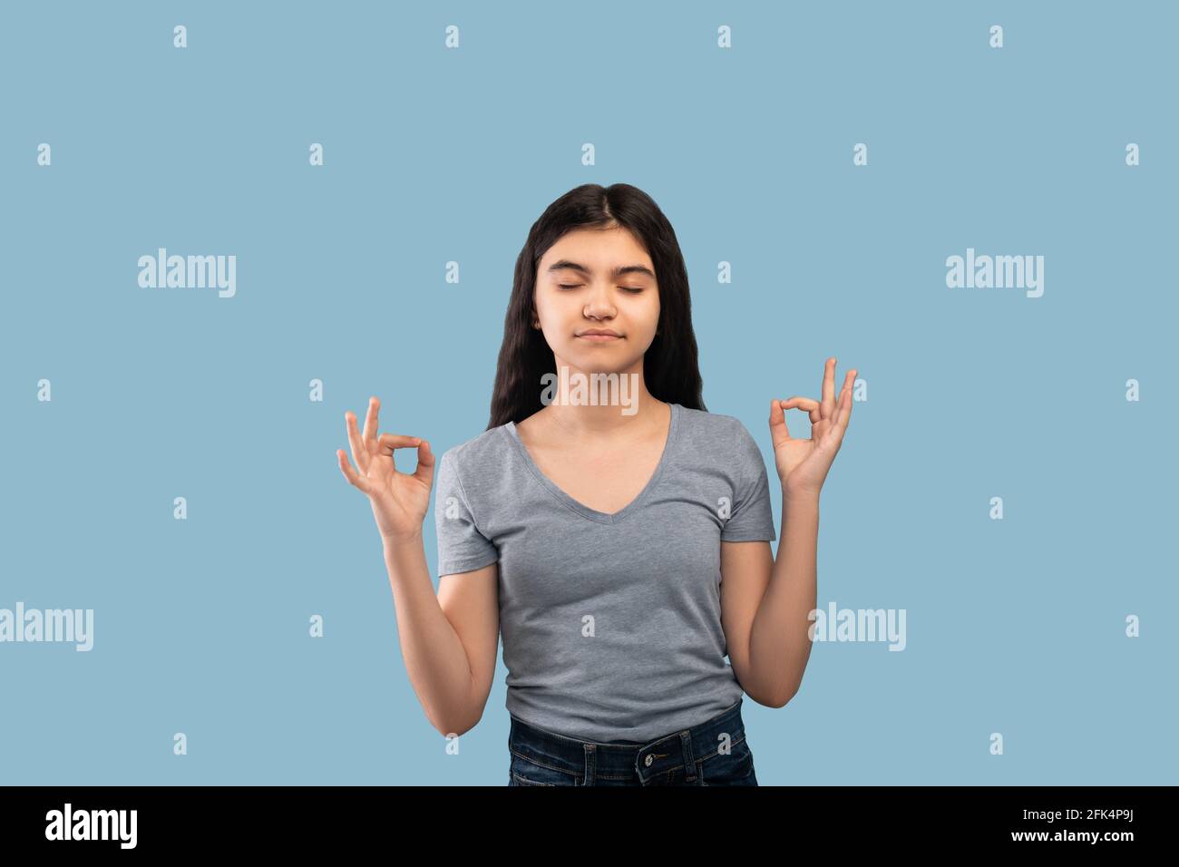Peaceful Indian teen girl meditating with closed eyes over blue studio background Stock Photo