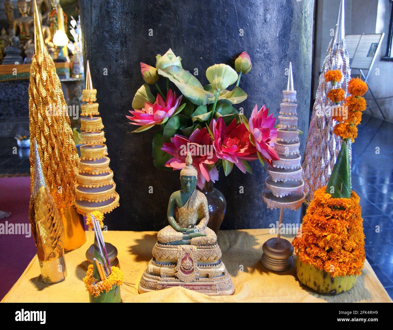 Jade Buddha dressed in gold surrounded by prang shaped decorations and lotus blossoms. Stock Photo