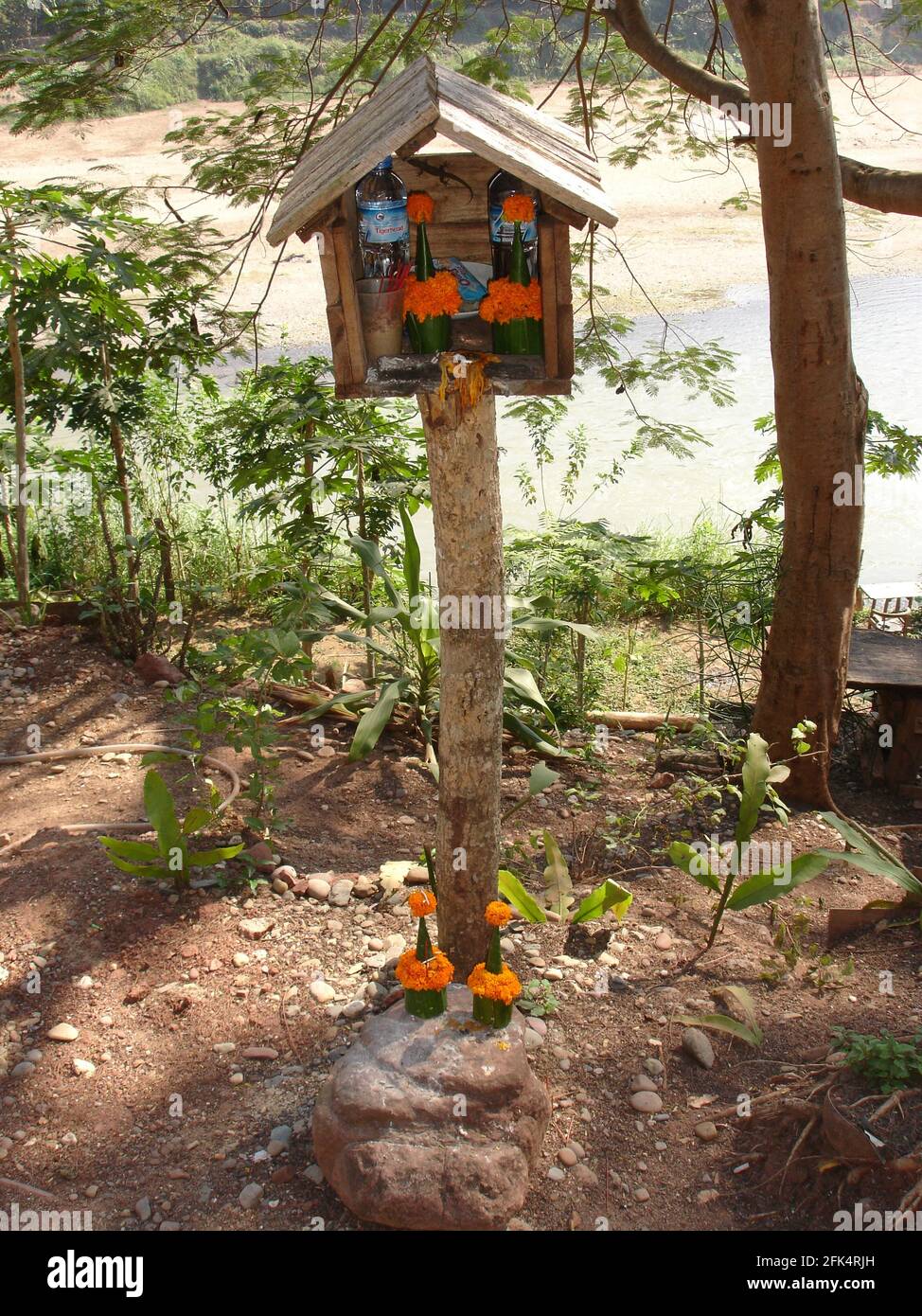 Riverside spirit house with water, food and marigolds for the spirits to ensure protection against malevolent forces.. Stock Photo