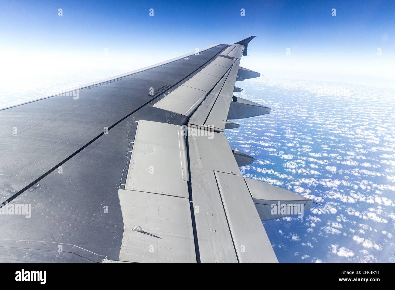 The view from the window of a jet aircraft wing looking down on a blue sky with fluffy white clouds Stock Photo
