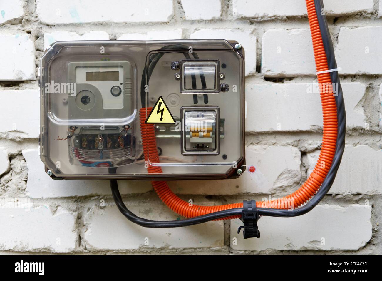 Closeup electrical power supply box with counter, fuses and switch with a transparent plastic cover on a old white brick wall Stock Photo