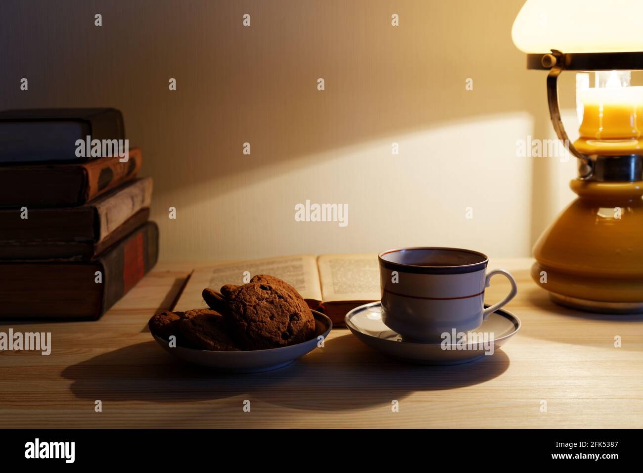 Cup of tea and stack of old books on the table with warm lighting lamp Stock Photo