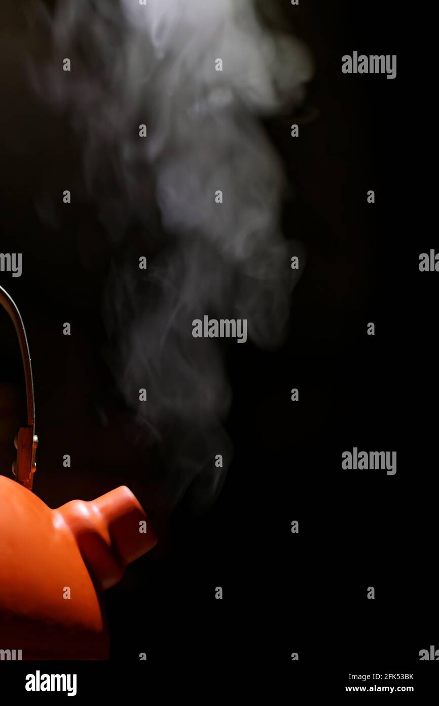 Orange kettle with boiling water and steam escaping from the spout against black background. Stock Photo