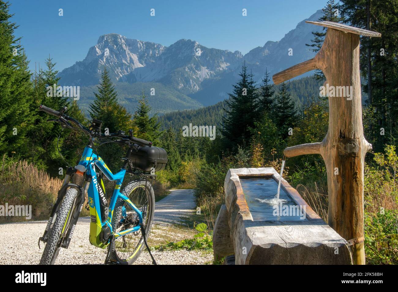 Das E-Bike vor dem Holzbrunnen - Otto Brunn - auf dem Weg zur Stoißer Alm  auf dem Teisenberg mit dem Hochstaufen im Hintergrund Stock Photo - Alamy