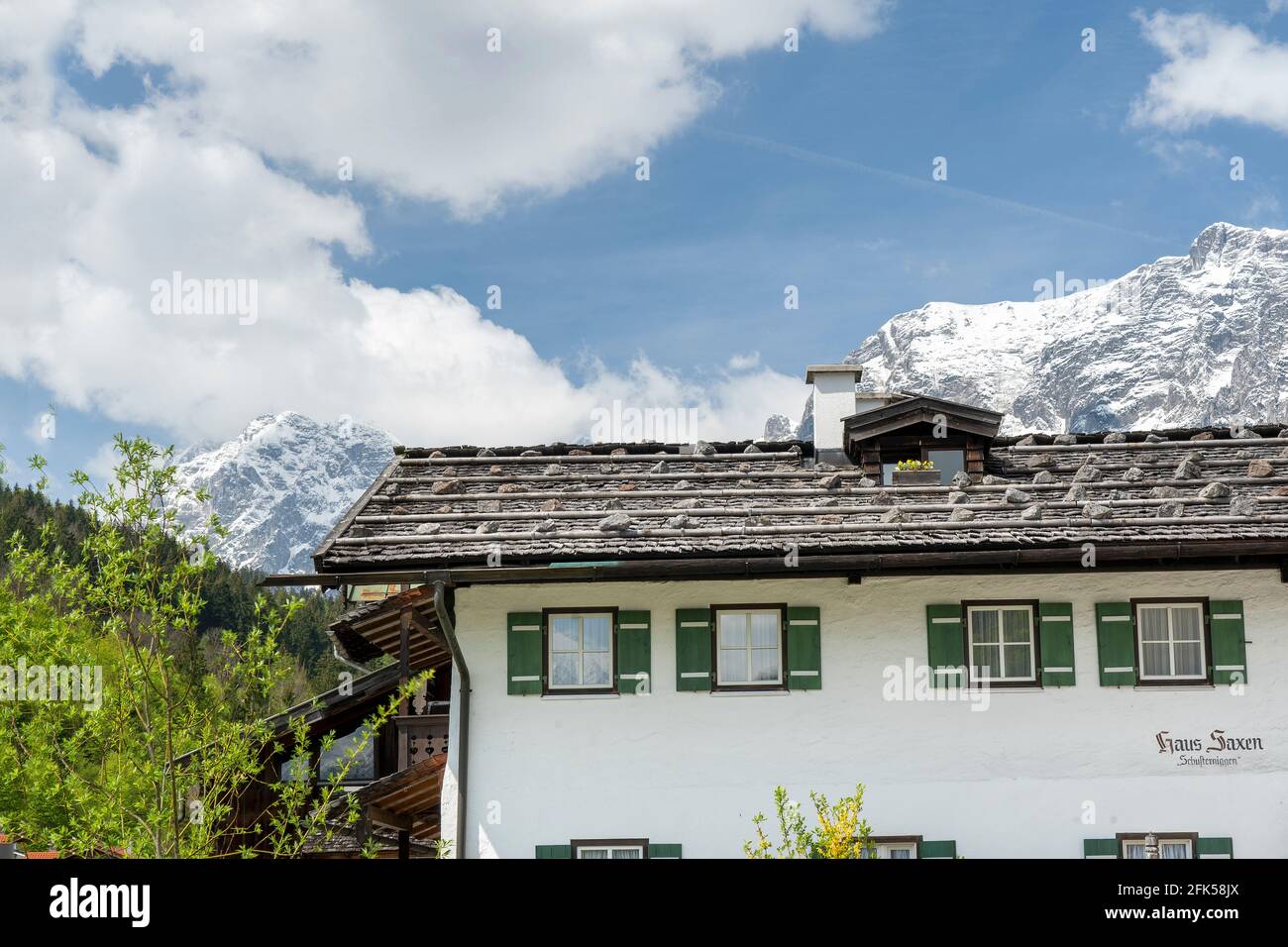 frühlingshaftes , mit Holzschnindeln gedecktes Haus mit der noch winterlichen Reiter Alpe in der Ramsau - Berchtesgadener Land Stock Photo
