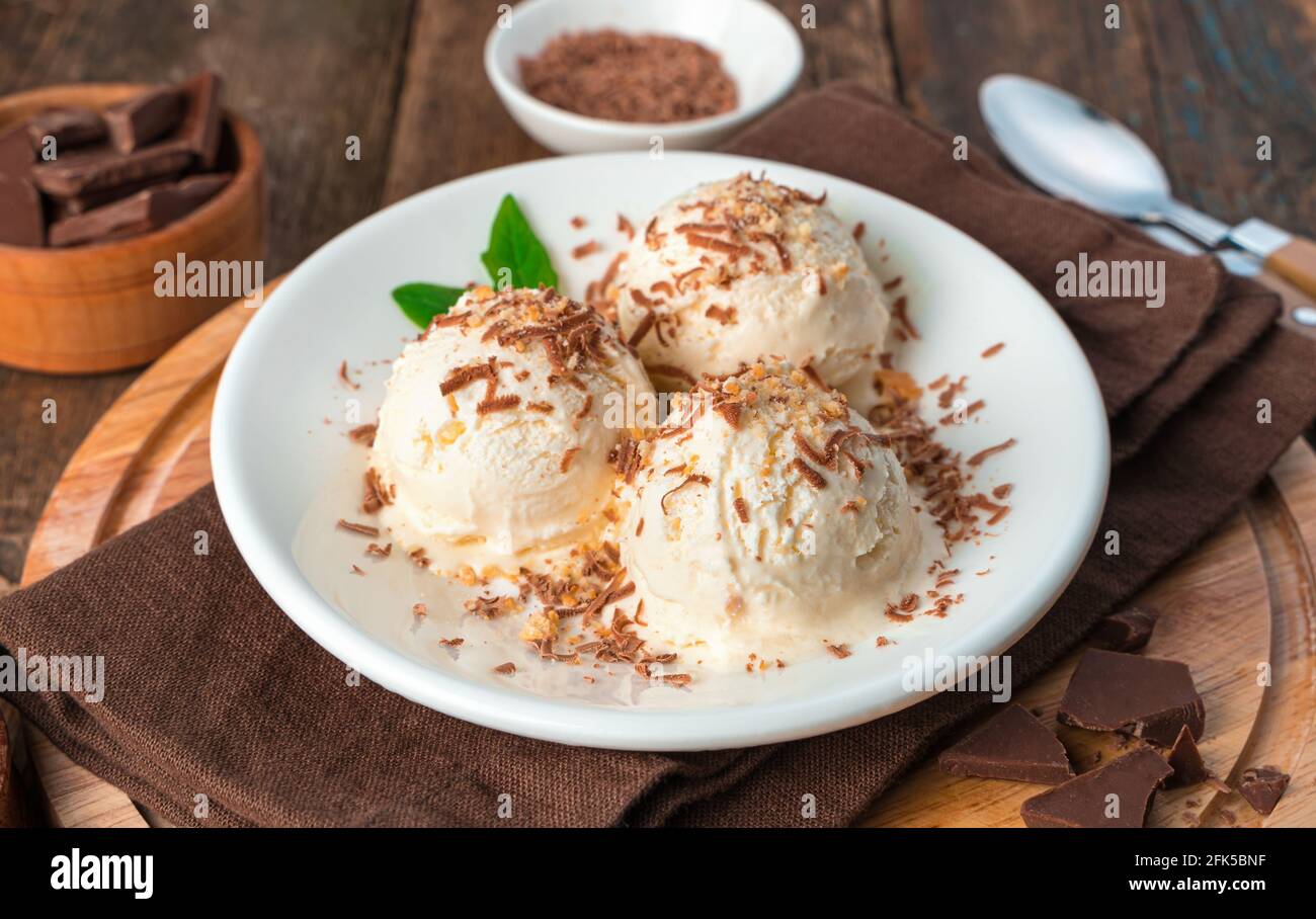 Three balls of ice cream close-up in a white plate on a brown background. Stock Photo