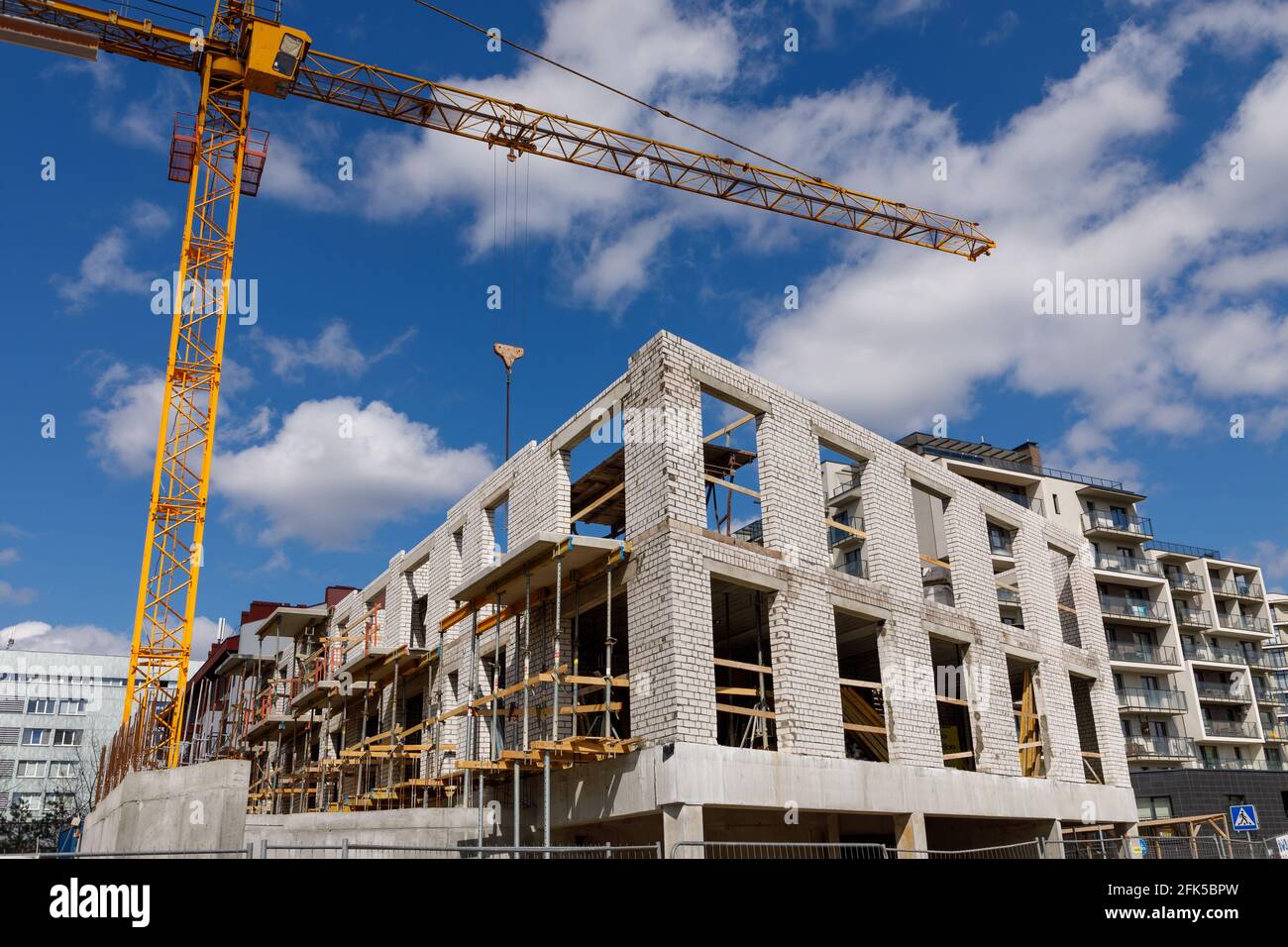Unfinished construction of a multi-store residential brick building and a tall crane. The photo is taken in Vilnius, Lithuania. Stock Photo