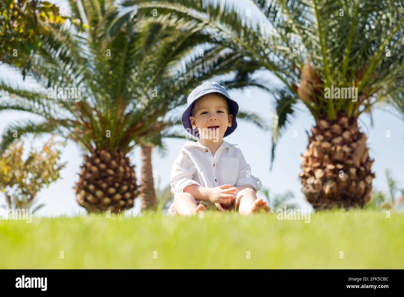 Happy little boy laying on green grass under palms Stock Photo
