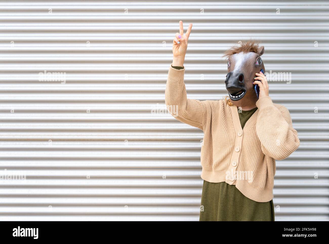 Female portrait wearing horse head mask talking on phone with two fingers up,victory sign.Woman success ,celebration concept,advertisement lifestyle w Stock Photo