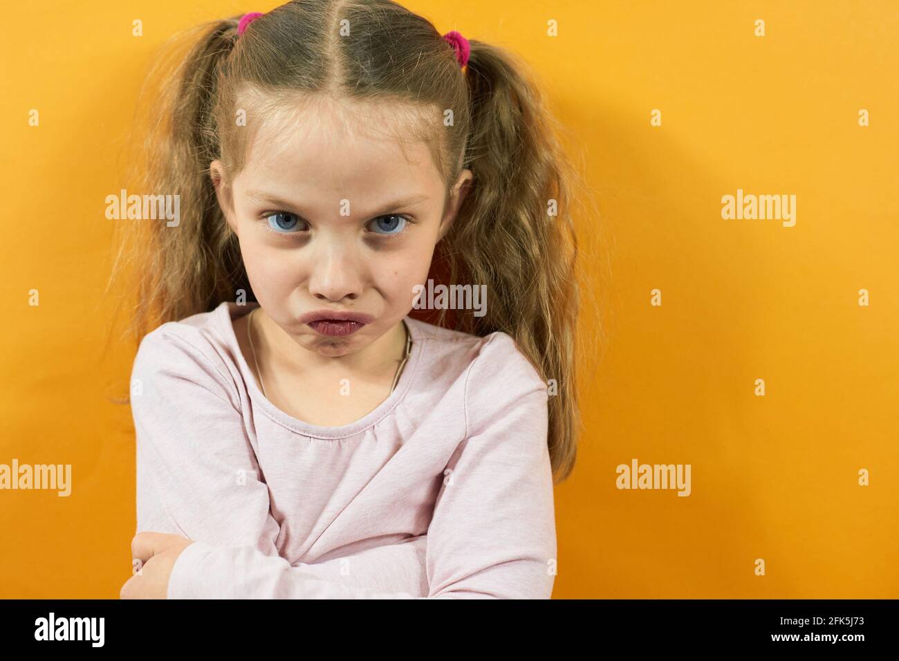portrait of an angry little girl on a yellow background, emotions in children. Stock Photo