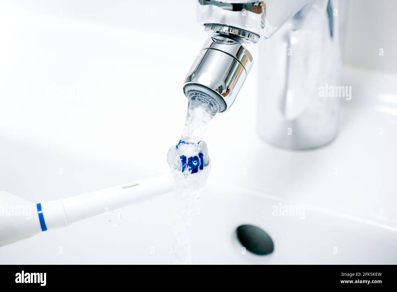 Cleaning An Electric Toothbrush Under Pouring Water At Bathroom Sink Stock Photo