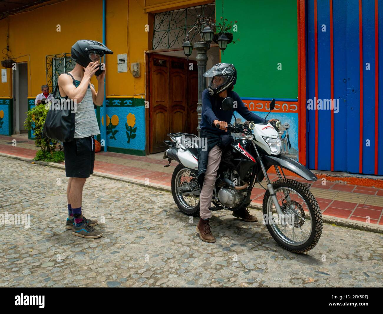 Guatapé, Antioquia, Colombia - April 4 2021: Woman Riding a Motorcycle and a Young White Man Getting on Behind Her Stock Photo