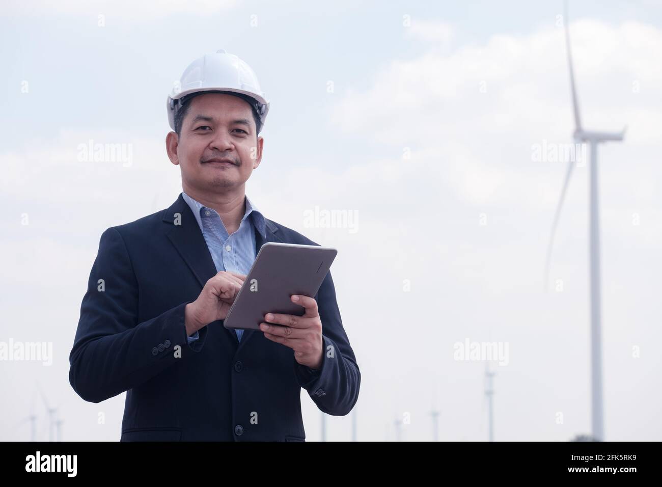 Successful engineer windmills manager standing and hoding tablet with wind turbine in background Stock Photo