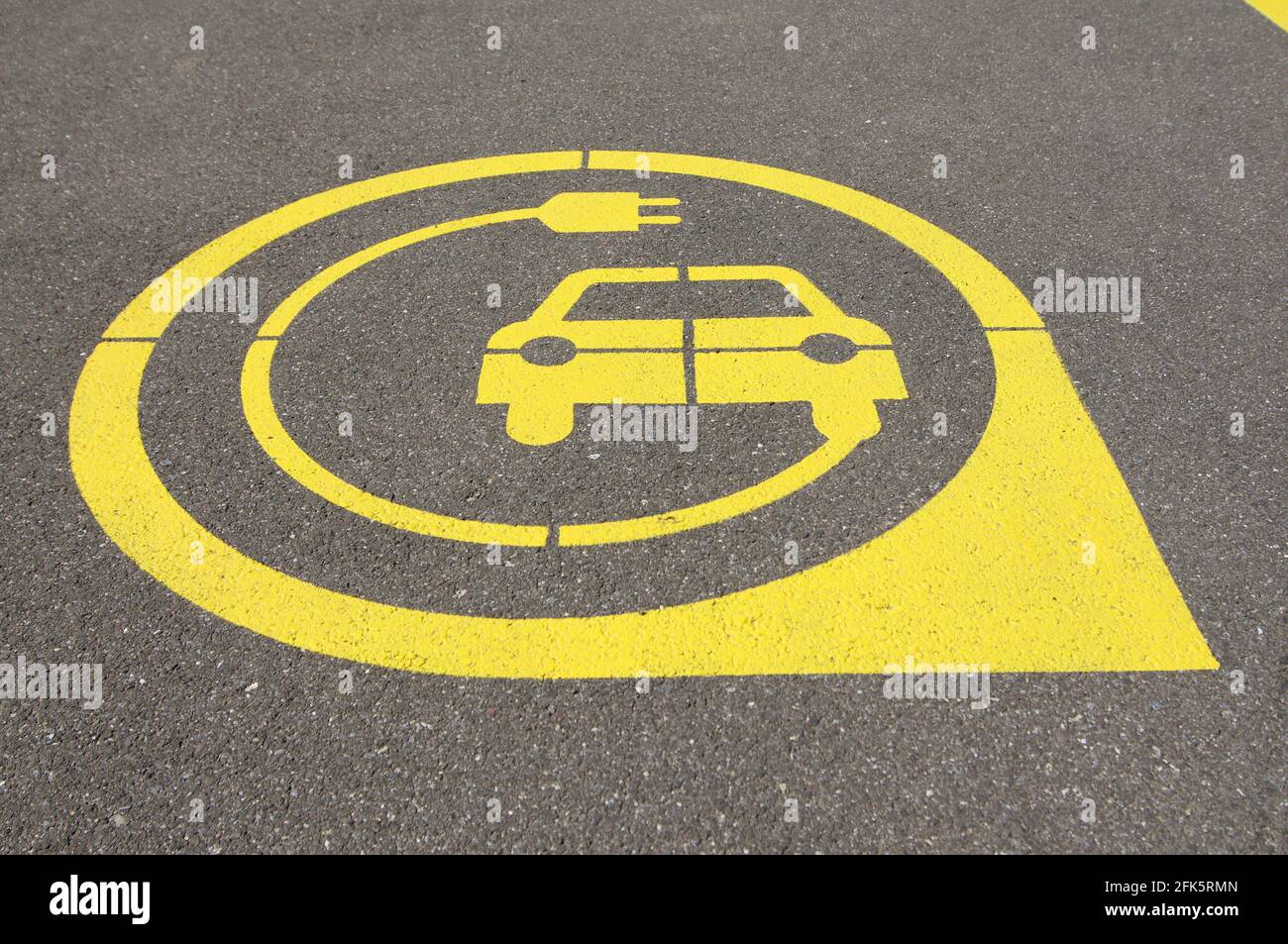 low angle view on yellow electric vehicle charging station symbol on black asphalt located in the city of Zug, Switzerland Stock Photo