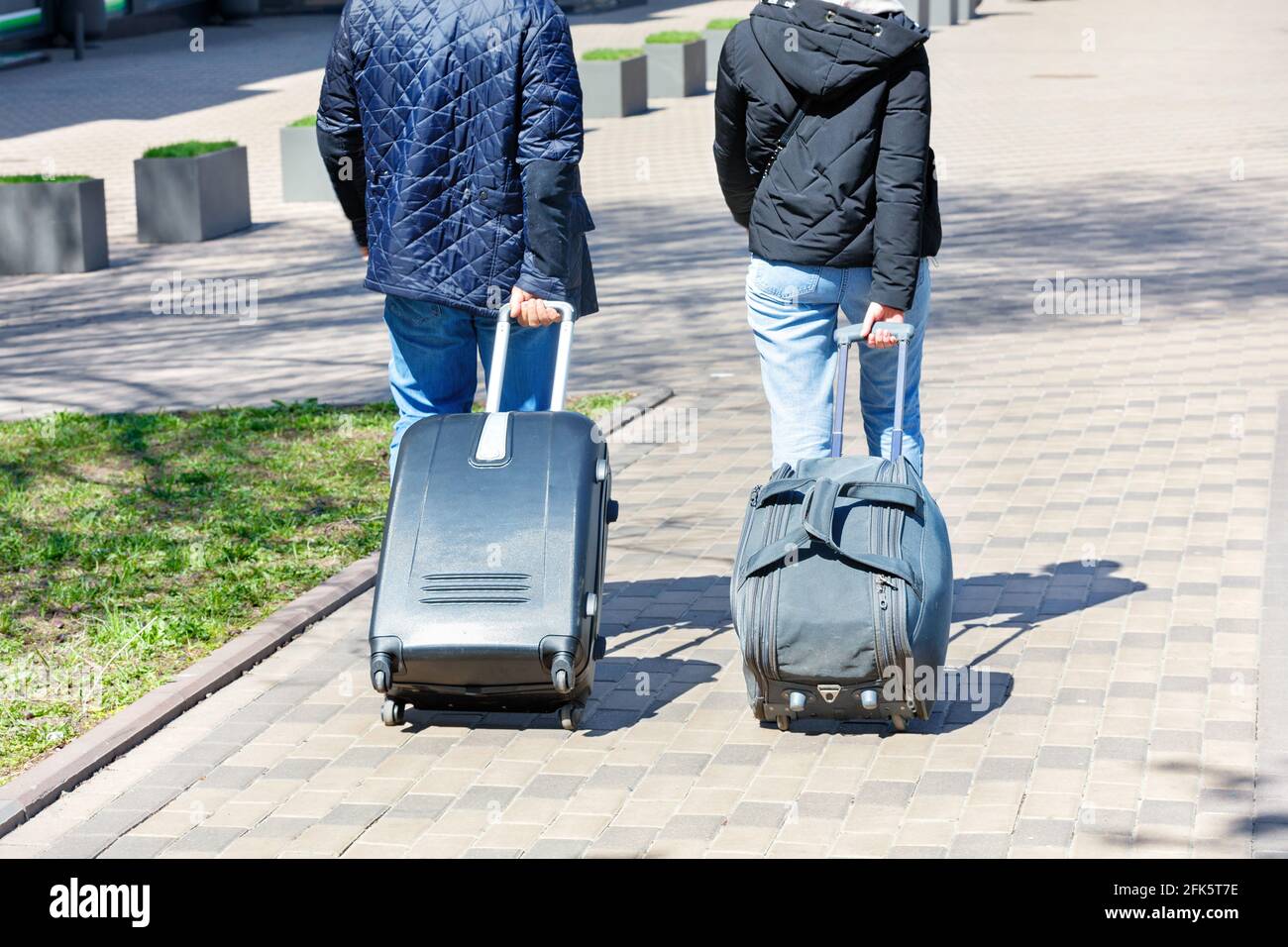 Two people, a man and a woman, walk along the cobbled sidewalk, carrying a  travel bag and a suitcase on wheels behind them Stock Photo - Alamy