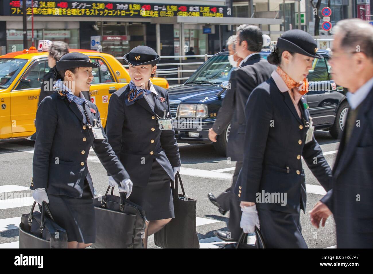 Three female off duty flight attendants wearing uniforms crossing busy zebra crossing in Ginza, Tokyo, Japan Stock Photo