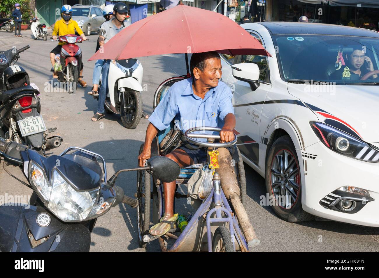 Vietnamese Man with wooden leg wheeling himself along the street in a