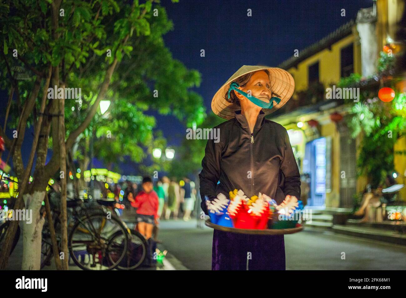 Elderly Vietnamese lady sells colourful floating lanterns by the riverside at dusk, Old Town, Hoi An, Vietnam Stock Photo
