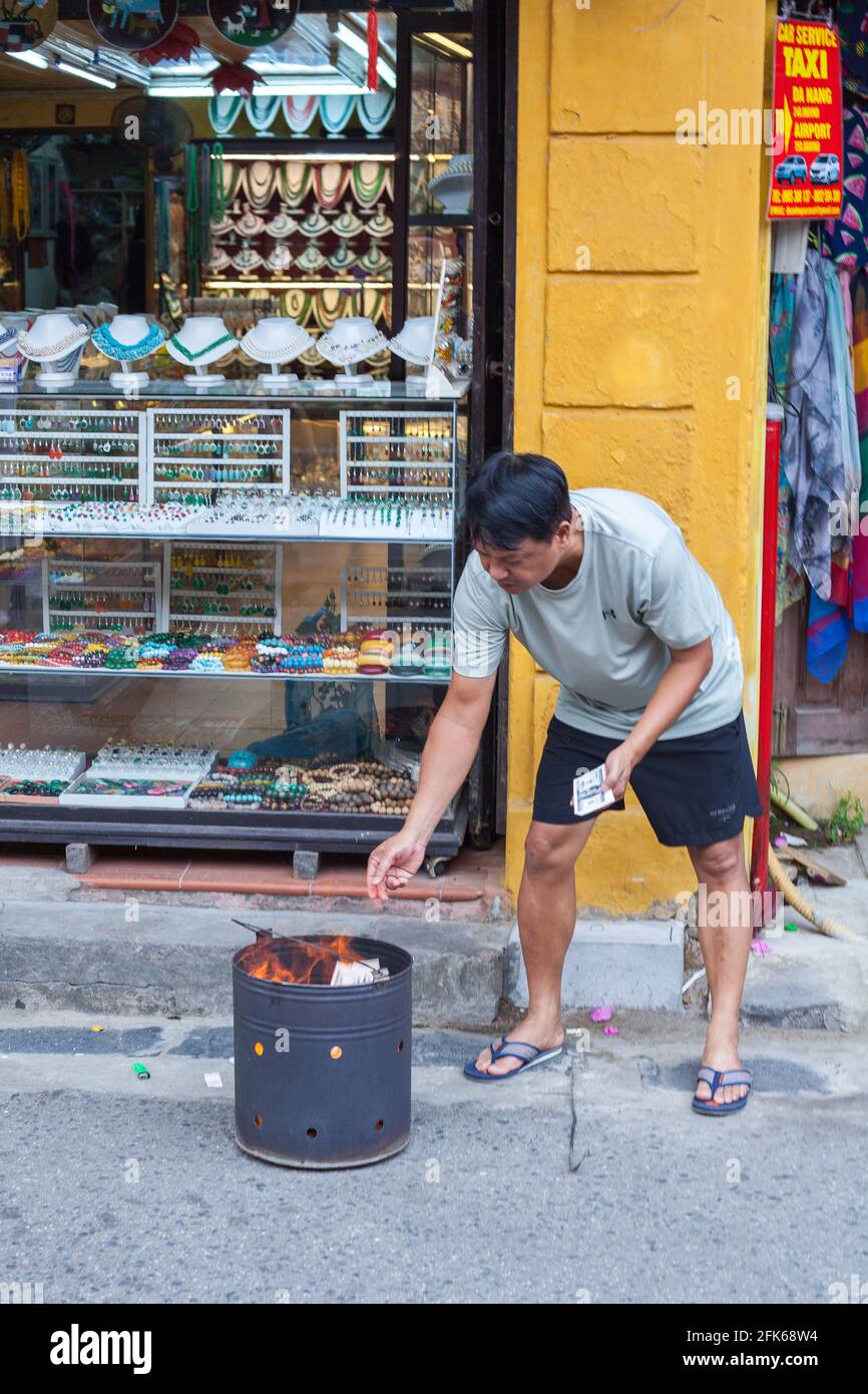 Middle aged Vietnamese male burning votive/ghost/spirit paper money on the street, Old Town, Hoi An, Vietnam Stock Photo