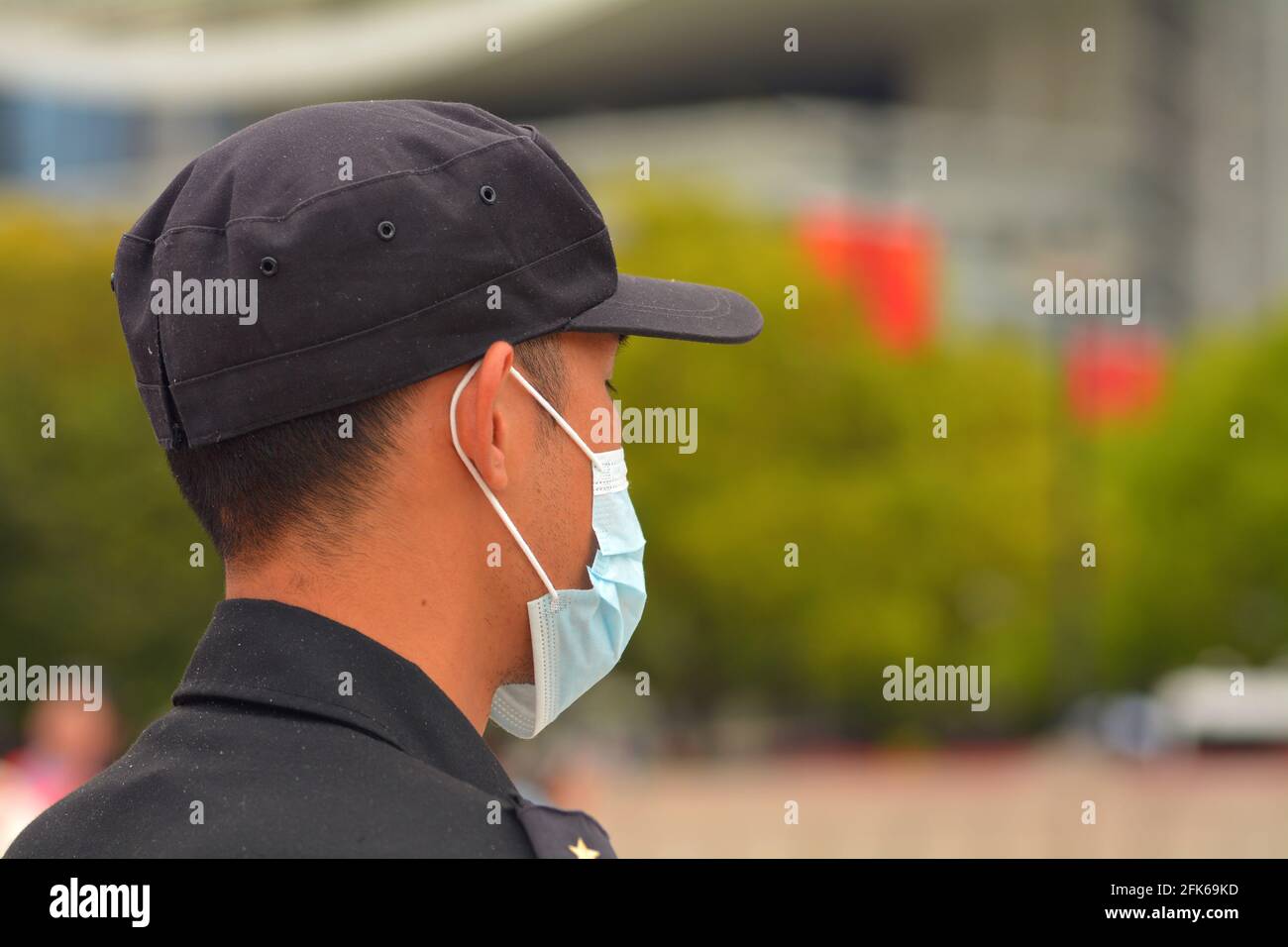 Security guard wearing a correctly fitted medical mask watching people in a Chinese park Stock Photo