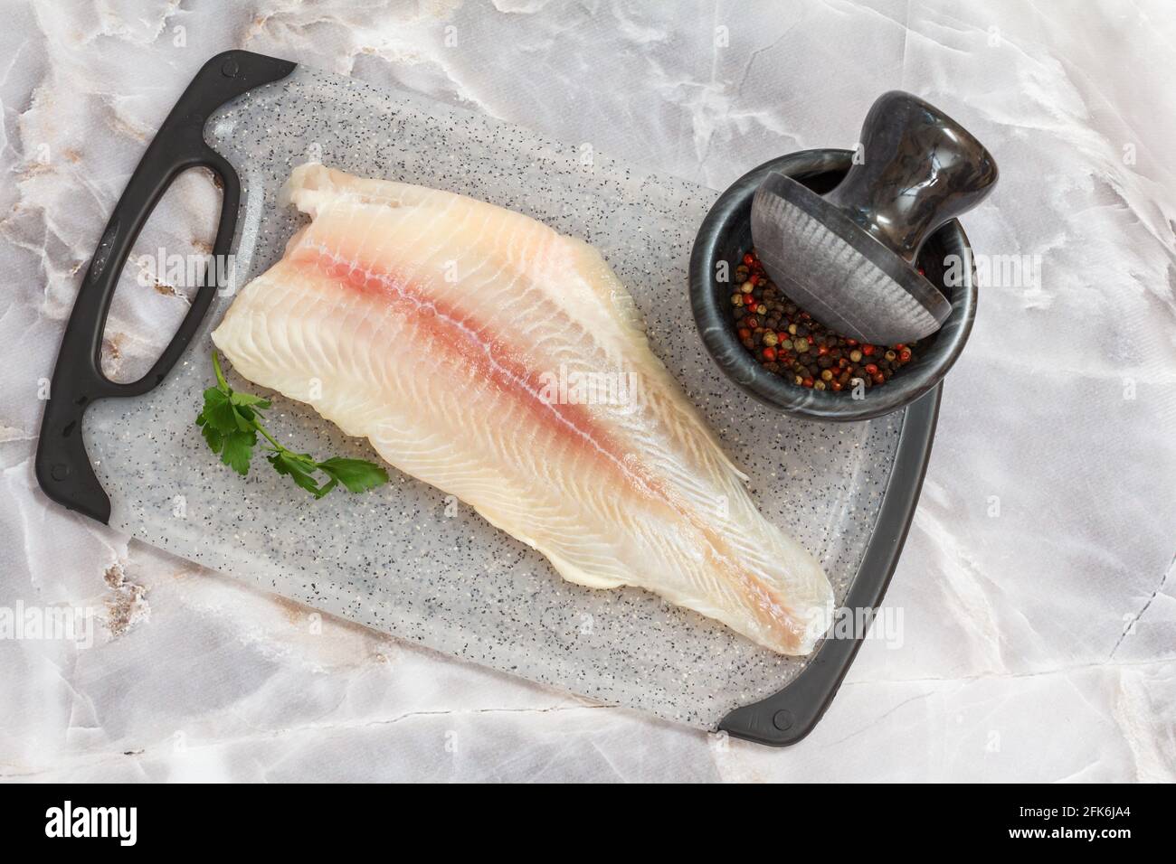 Fillet of raw pangasius fish with parsley leaves and spices on a cutting board laying on the stone kitchen table. Top view. Stock Photo