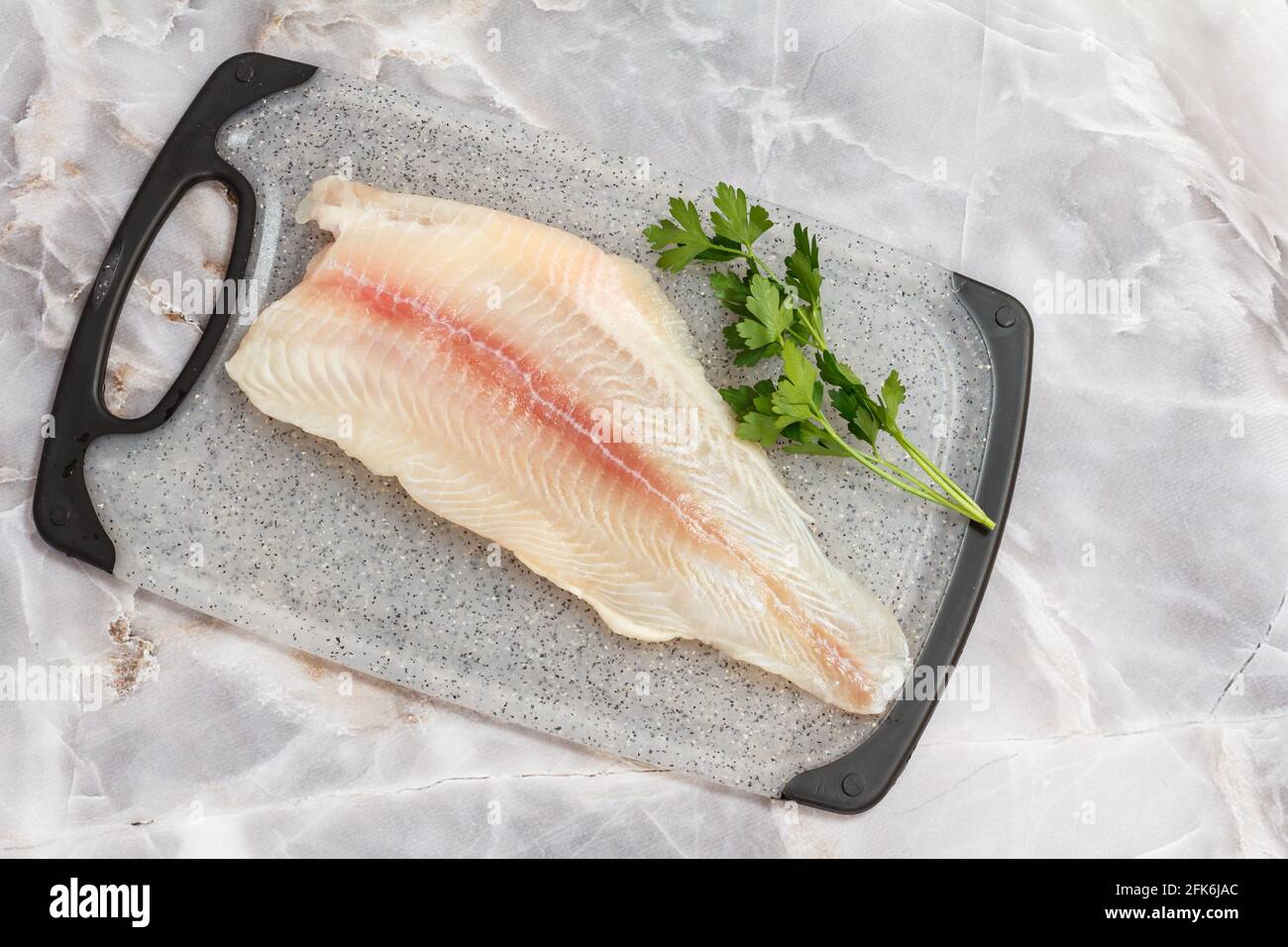 Fillet of raw pangasius fish with parsley leaves on cutting board. Top view. Stock Photo