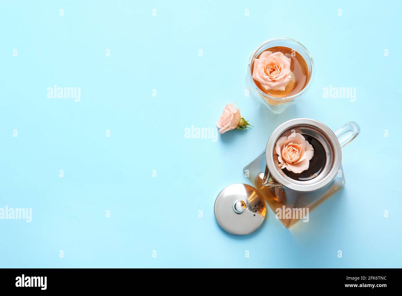 Teapot with hot tea, glass and rose flowers on color background Stock
