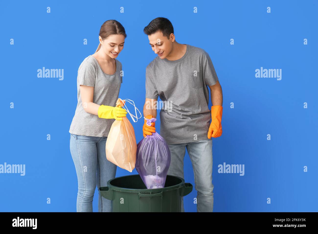 Young couple throwing garbage in trash bin on color background Stock